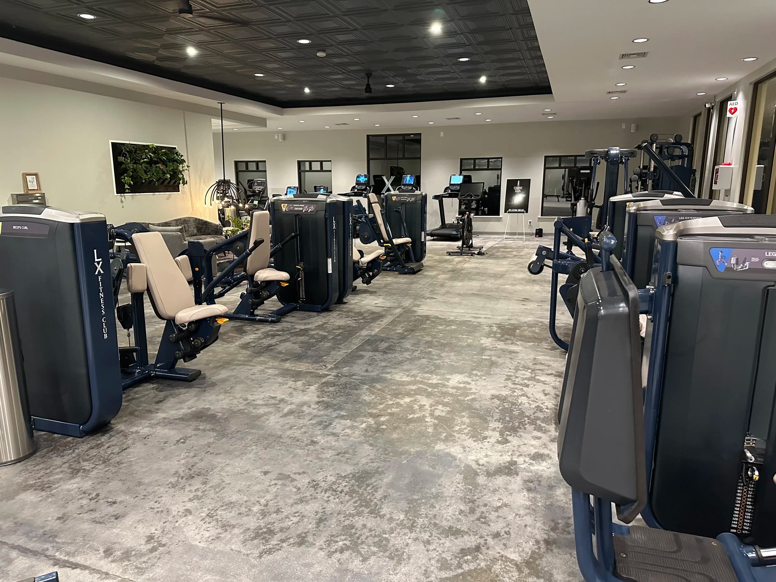 The main training floor at LX Fitness Club, lined with navy LX-branded selectorized machines beneath a black coffered ceiling.
