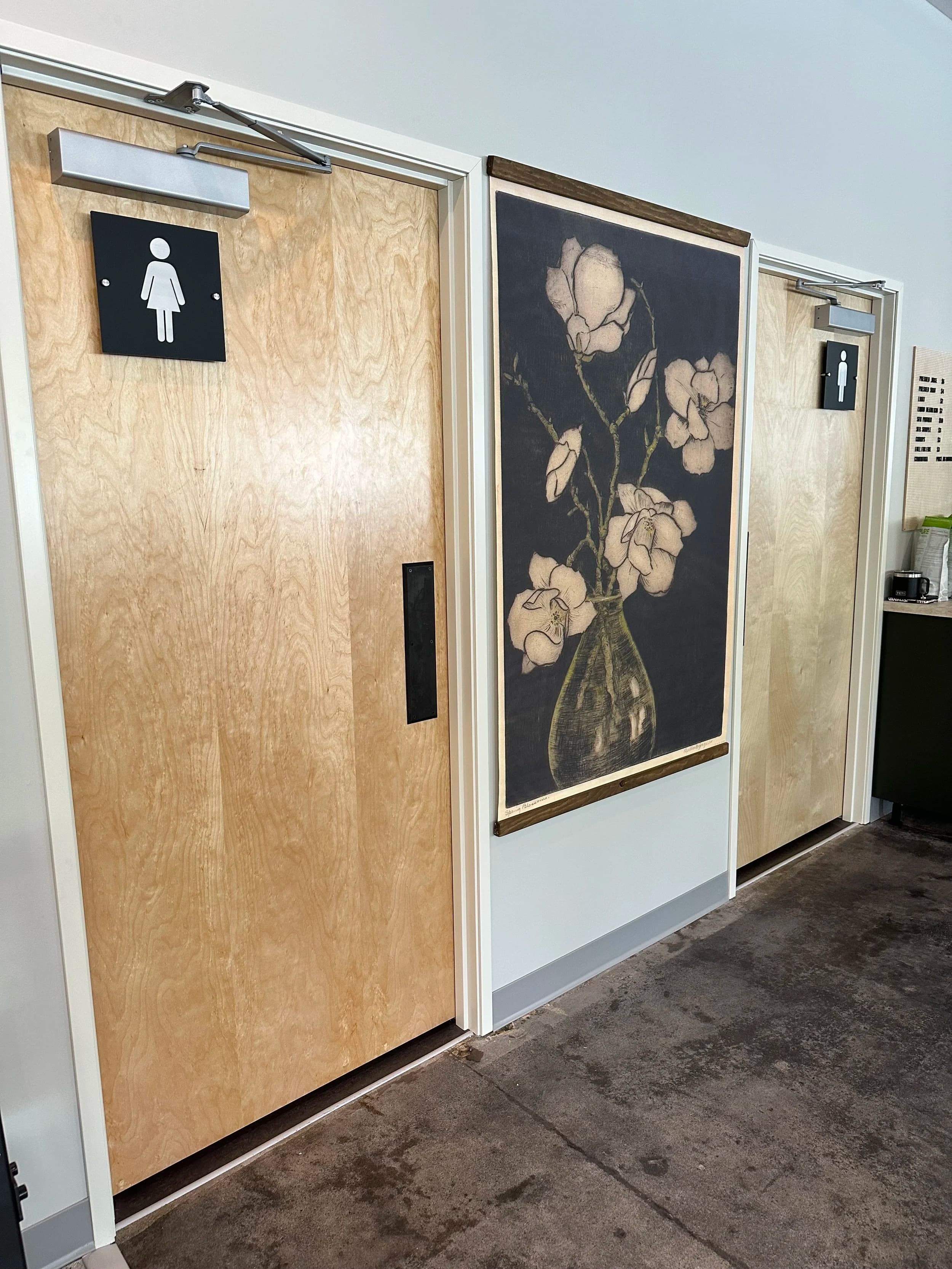 The corridor to the locker rooms at LX Fitness Club, with pale birch doors and a framed botanical woodblock print.